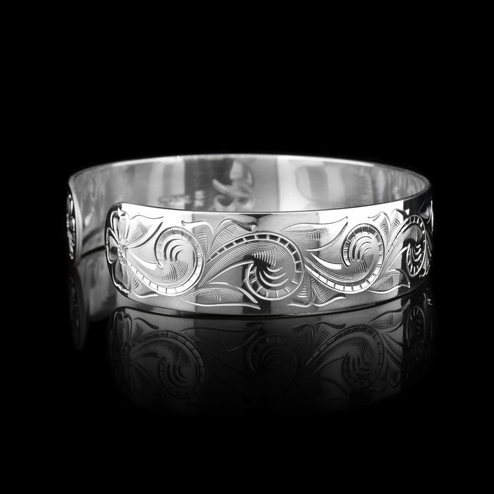 This sterling silver bracelet cuff has a wide band with carvings depicting designs across the band and a bear. The bear is made of 10K gold.