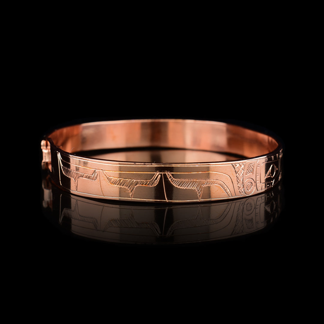 A Copper Hummingbird bracelet bangle that depicts two Hummingbird faces facing eachother with a flower in between them. The bodies of the Hummingbirds are engraved on the rest of the bracelet.