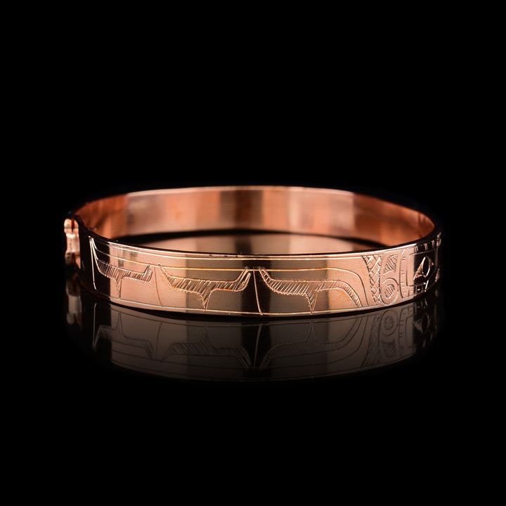 A Copper Hummingbird bracelet bangle that depicts two Hummingbird faces facing eachother with a flower in between them. The bodies of the Hummingbirds are engraved on the rest of the bracelet.