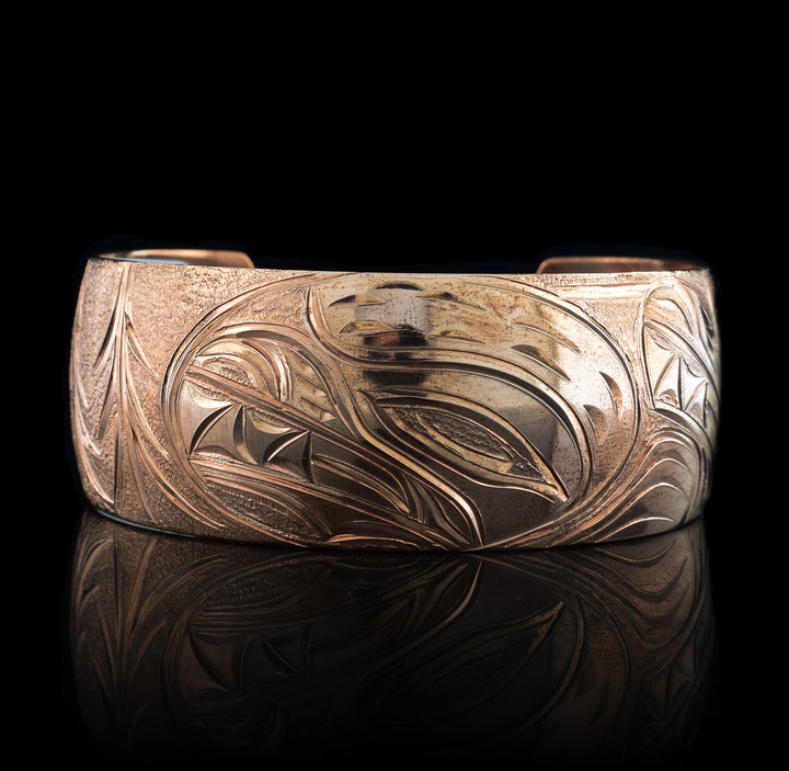 This stunning Bear bracelet is made using copper and has a single, wide band with a gap in the back. In the center of the band, there is the head of the Baby Bear placed in the middle of an oval design which represents the womb. On the right end of the band, the mother Bear is depicted with the side profile of her head which is tilted upwards. On the other end of the band there are simple pine trees carved into the band