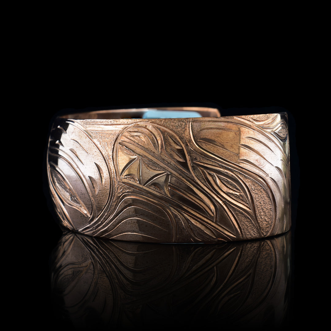 This stunning Bear bracelet is made using copper and has a single, wide band with a gap in the back. In the center of the band, there is the head of the Baby Bear placed in the middle of an oval design which represents the womb. On the right end of the band, the mother Bear is depicted with the side profile of her head which is tilted upwards. On the other end of the band there are simple pine trees carved into the band