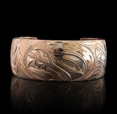 This stunning Bear bracelet is made using copper and has a single, wide band with a gap in the back. In the center of the band, there is the head of the Baby Bear placed in the middle of an oval design which represents the womb. On the right end of the band, the mother Bear is depicted with the side profile of her head which is tilted upwards. On the other end of the band there are simple pine trees carved into the band