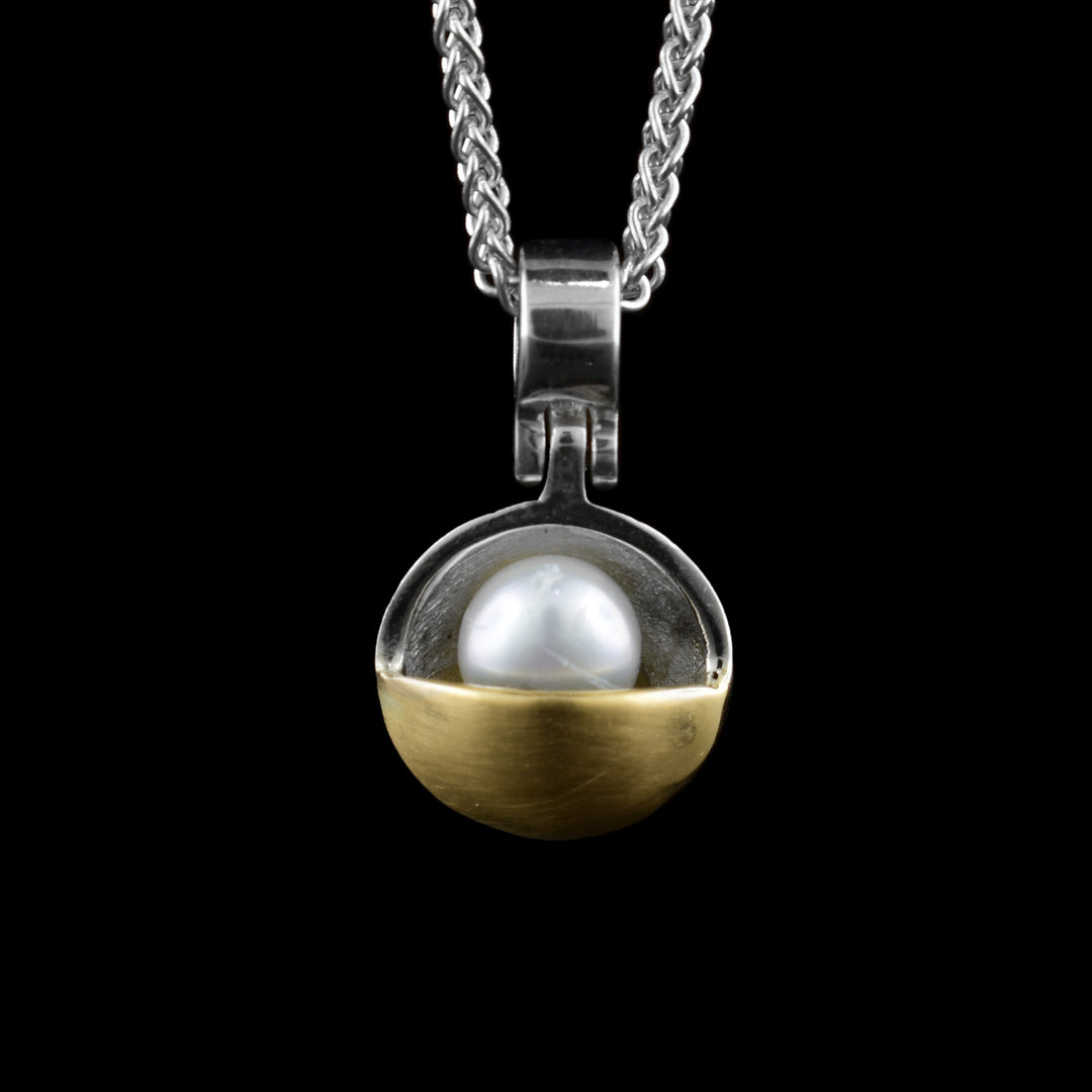 This gold pearl pendant has a concave sterling silver circle with a pink pearl in it. Half of the circle is covered by 14K gold that also covers some of the piece. The pendant dangles on a hinge from the bail.