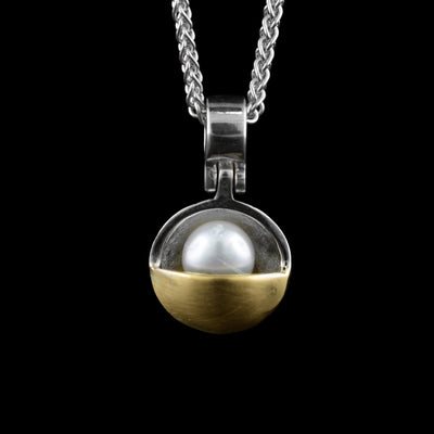 This gold pearl pendant has a concave sterling silver circle with a pink pearl in it. Half of the circle is covered by 14K gold that also covers some of the piece. The pendant dangles on a hinge from the bail.