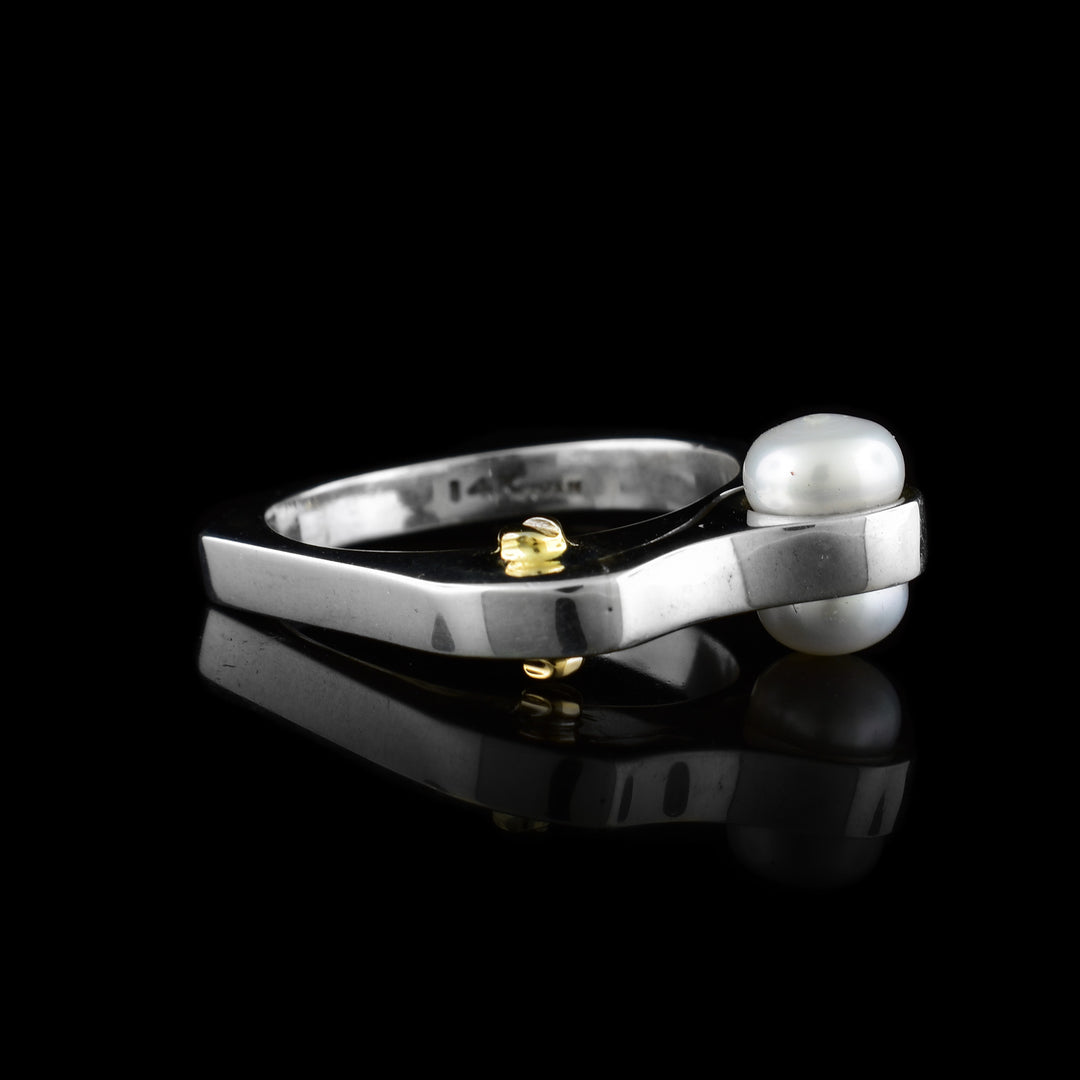 This abstract sterling silver ring has a thin signet along the top half of the ring. Embedded in the signet are two fresh water pearls and a 14K gold stud.