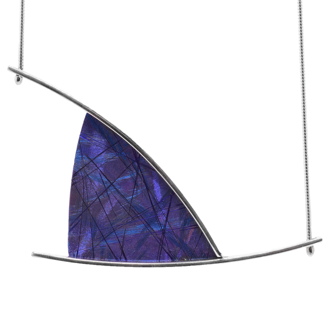 This abstract titanium necklace with pendant has been made from sterling silver and anodized titanium. There is a triangle shaped titanium piece that is held between silver wires that extend past the piece. There is a light blue color and deeper blue/purple designs on the surface of the titanium piece that are achieved by anodizing the metal.
