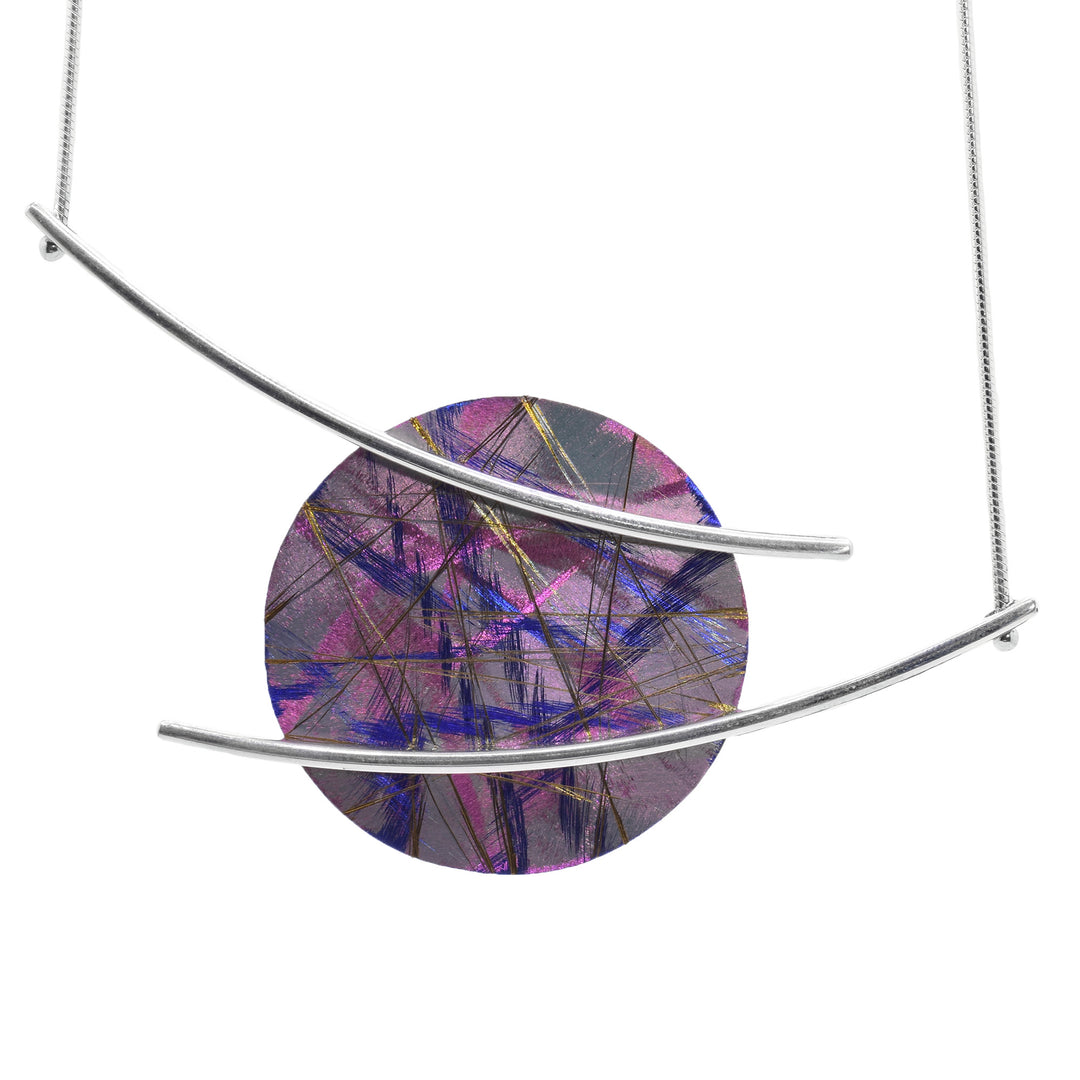 This anodized titanium pendant necklace has a large, titanium pendant with a circle shape. There are long, horizontal and curved pieces of sterling silver that are connected to the front of the pendant and extend out to attach to the necklace chain. There are blue, pink and gold designs on the titanium piece of the necklace.