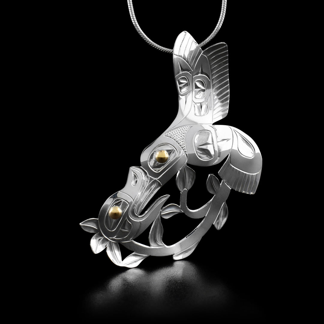 This hummingbird necklace has a hummingbird mid-flight drinking from a flower with a long stem and leaves. Parts of the pendant have been cut out.