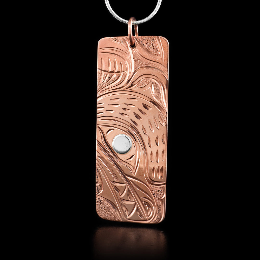 This Bear pendant is a rectangular shape and depicts the head of a bear facing downwards with a short snout and teeth showing. Its eye has been made from silver. Above its head is its ear and paw.