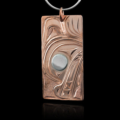 This wolf pendant is rectangular in shape and depicts the head of a wolf with a short snout and its teeth showing facing down. Its eye is silver while the rest is copper. Behind the head of the wolf is its large paw.