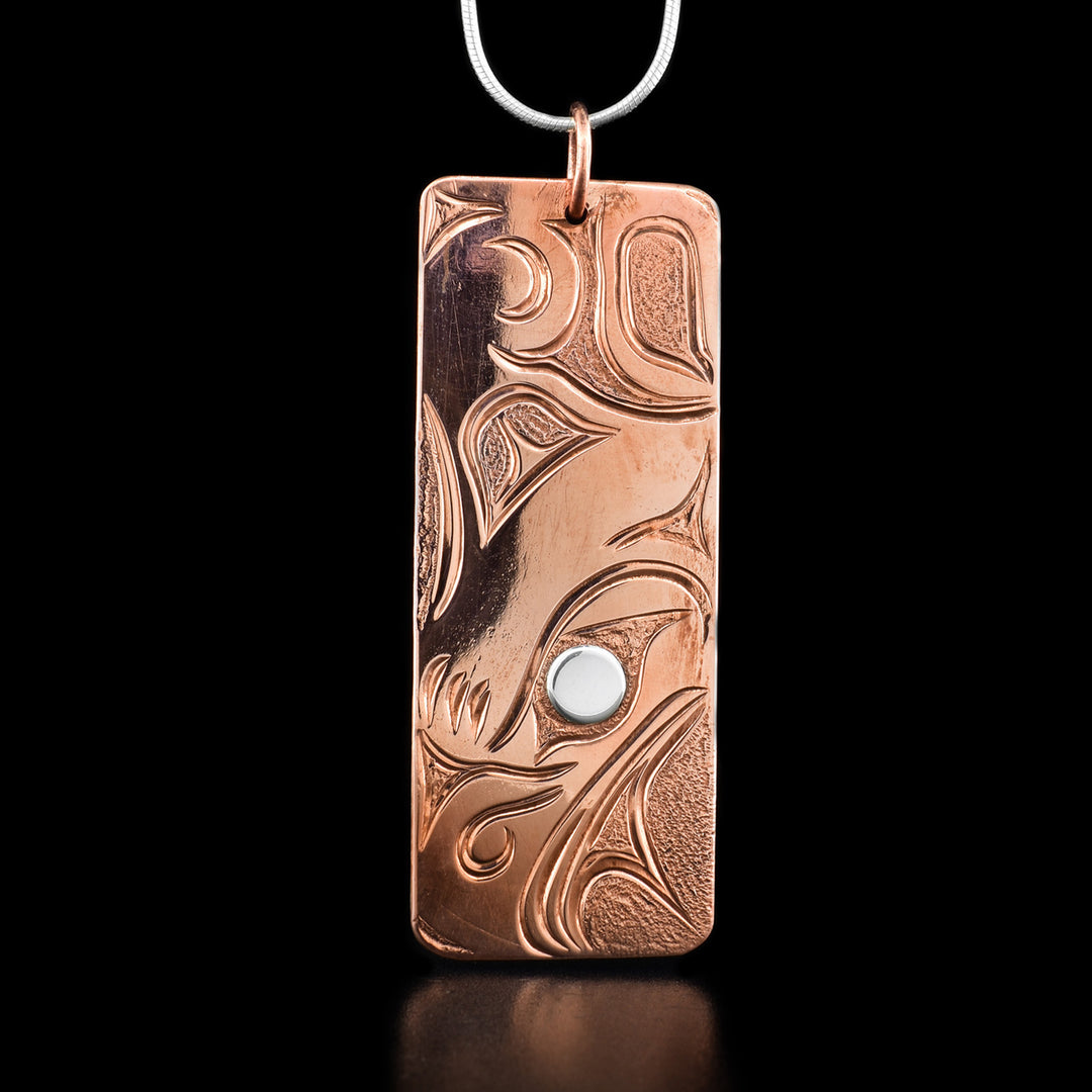 This thunderbird necklace depicts the head of a thunderbird facing downward with a pointy beak and a large feather on its head. Its eye is made from silver while the rest is copper. Behind its head is it wing.