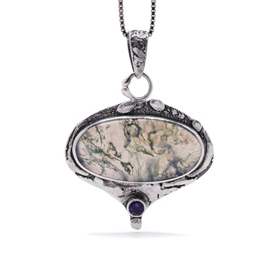 This moss agate pendnat is oval in shape with a large bail. It has oxidized sterling silver accents throughout and a round iolite gemstone set in sterling silver at the bottom of the pendant.
