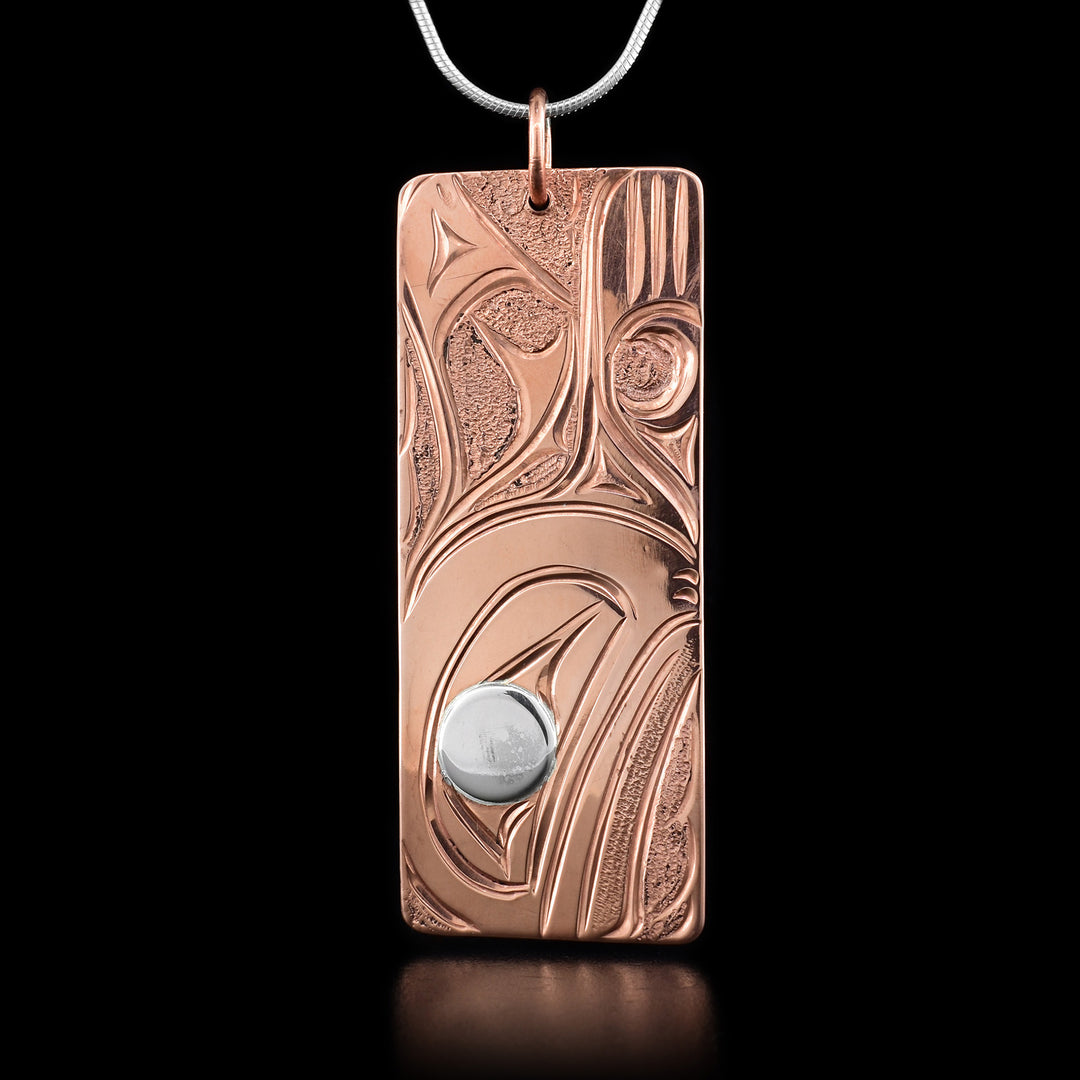 This whale necklace depicts the head of an orca facing down at the bottom of the pendant. Behind the head are the orca's dorsal fin and its flippers. The eye of the orca is silver while the rest is copper.