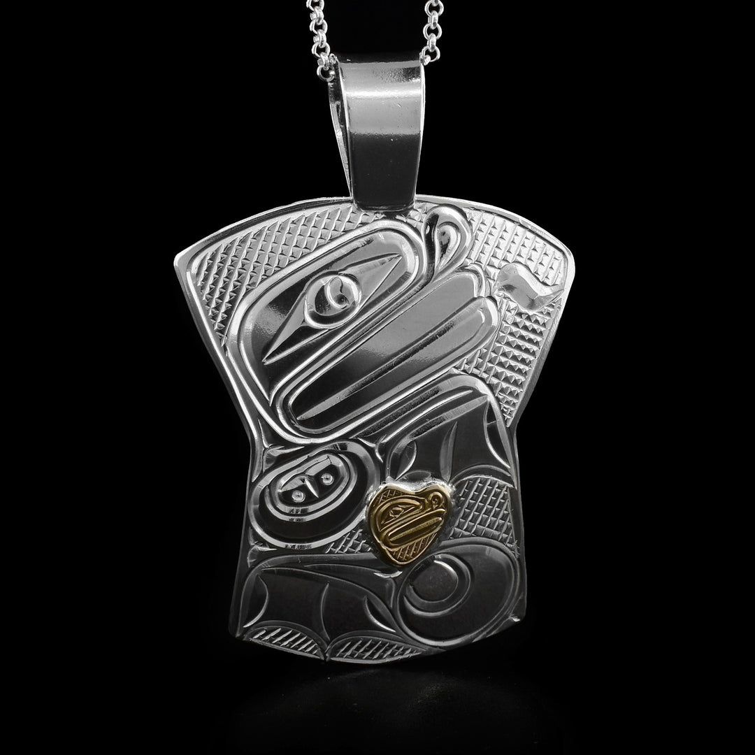 This frog pendant is in the shape of a shield with a large triangular bail at the top. The design depicts the head of a frog at the top with its tongue out and its body underneath. There is a small gold heart in the frog's body with a smaller frog head carved into it.