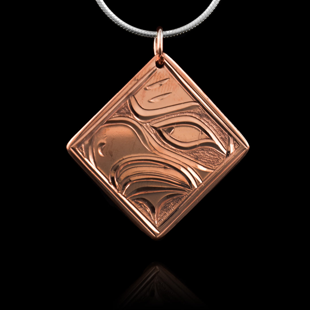 This copper Eagle pendant has a square, diamond shape. The head of the Eagle is carved into the piece at a side profile. Its eye and beak are shown and there are dimpled patterns around the scene.