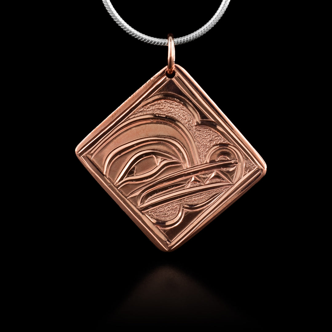 This copper Wolf pendant is square and diamond shaped. There is a thin border around the edges of the piece and the head of the Wolf legend is depicted in the center of it. The head is shown at a side profile with its eye, nose and teeth detailed. There are small dimpled textures in the back ground of the scene.