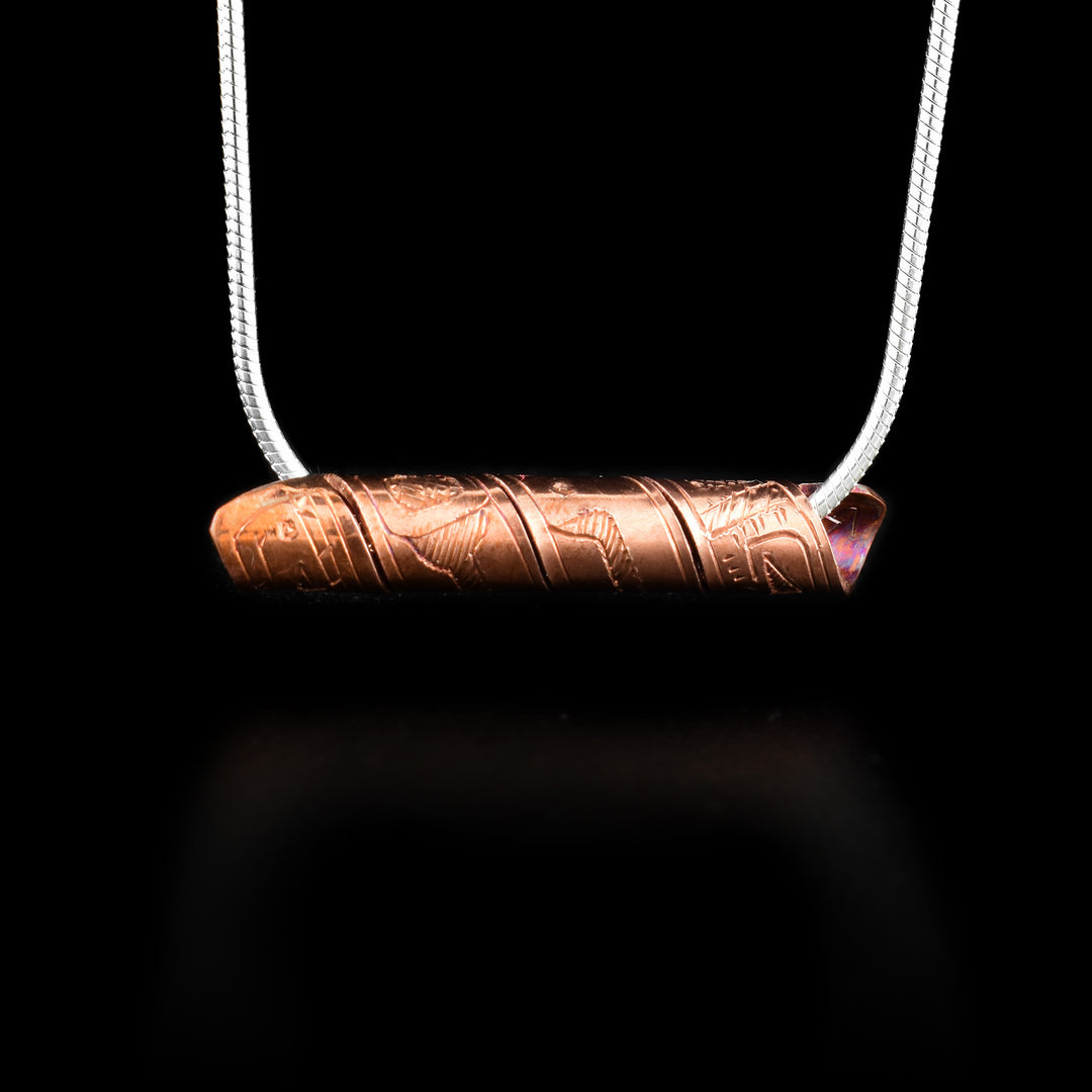 This spiral cylinder pendant is made from a single, copper band that has been twisted into a cylinder. There is depiction of the Orca legend carved into the surface of the band so it appears on the outside of the cylinder. It is shown at a side profile with its head, eye and mouth at one end and the rest of its body behind it.