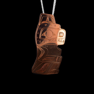 This copper Bear pedant is cutout in the shape of a Bear sitting upright. There are carvings on the piece depicting the Bear at a side profile. The eyed, teeth, nose, and clawed paws are detailed.
