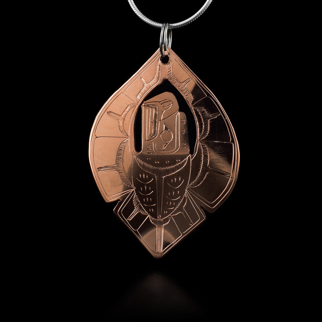 This teardrop pendant is made from copper and has a long, oval shape with both its ends making a point. The pendant is shaped like and Eagle with its wings reaching above it and its head is cutout in the center of it. There are also details carved into the piece detailing its beak and eyes as well as feather details on the wings and tail.