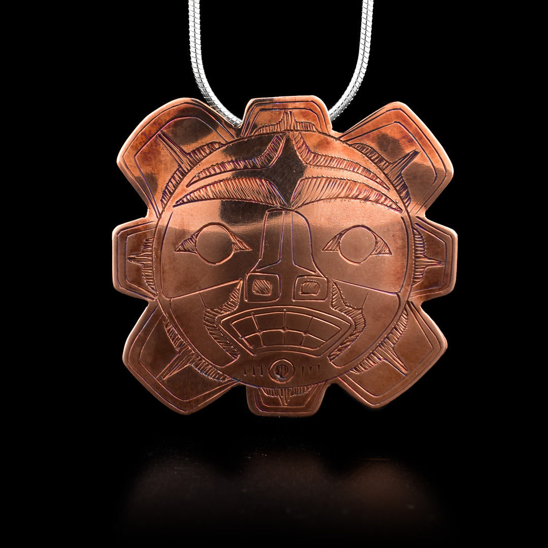 This copper Sun pendant is made from copper and has the shape of the Sun. There are eight, short and wide sun beams extending out from the circle shaped center and designs are carved into the surface of it. The eyes, eyebrows, nose, mouth and other details are shown.