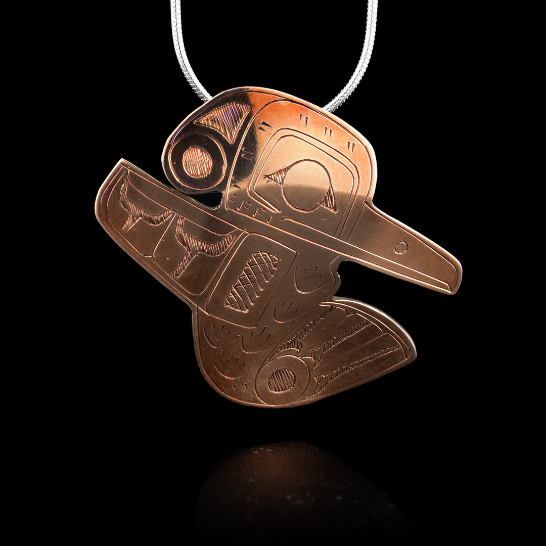 This Hummingbird pendant is made from copper and is shaped like the Hummingbird legend. The head is large and there is a small wing extending below the back of the head and its beak extends off the other side. At the bottom, its tail curves up and below the beak. There are designs carved into the piece showing the details of feathers across its body as well as its beak and eyes.