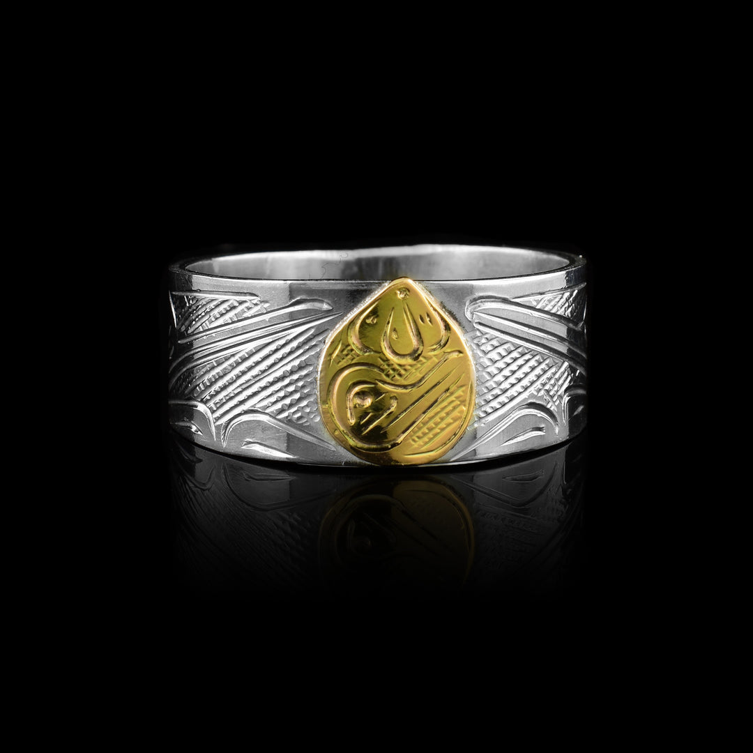 This two-tone band by artist Graham Henry is handcrafted from sterling silver and 10k gold. The design features a central Hummingbird legend hand-carved into a solid 10k gold inlay, complemented by additional Hummingbirds carved into the surrounding sterling silver band.