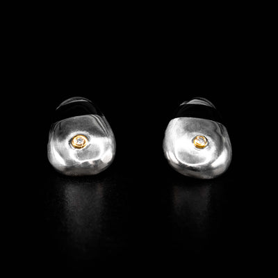 Sterling silver ovoidal stud earrings, each with a horizontal black strip of plexiglass across upper portion. Each earring has a diamond bezel set in 14K yellow gold on bottom portion. By Ivan Dobren.