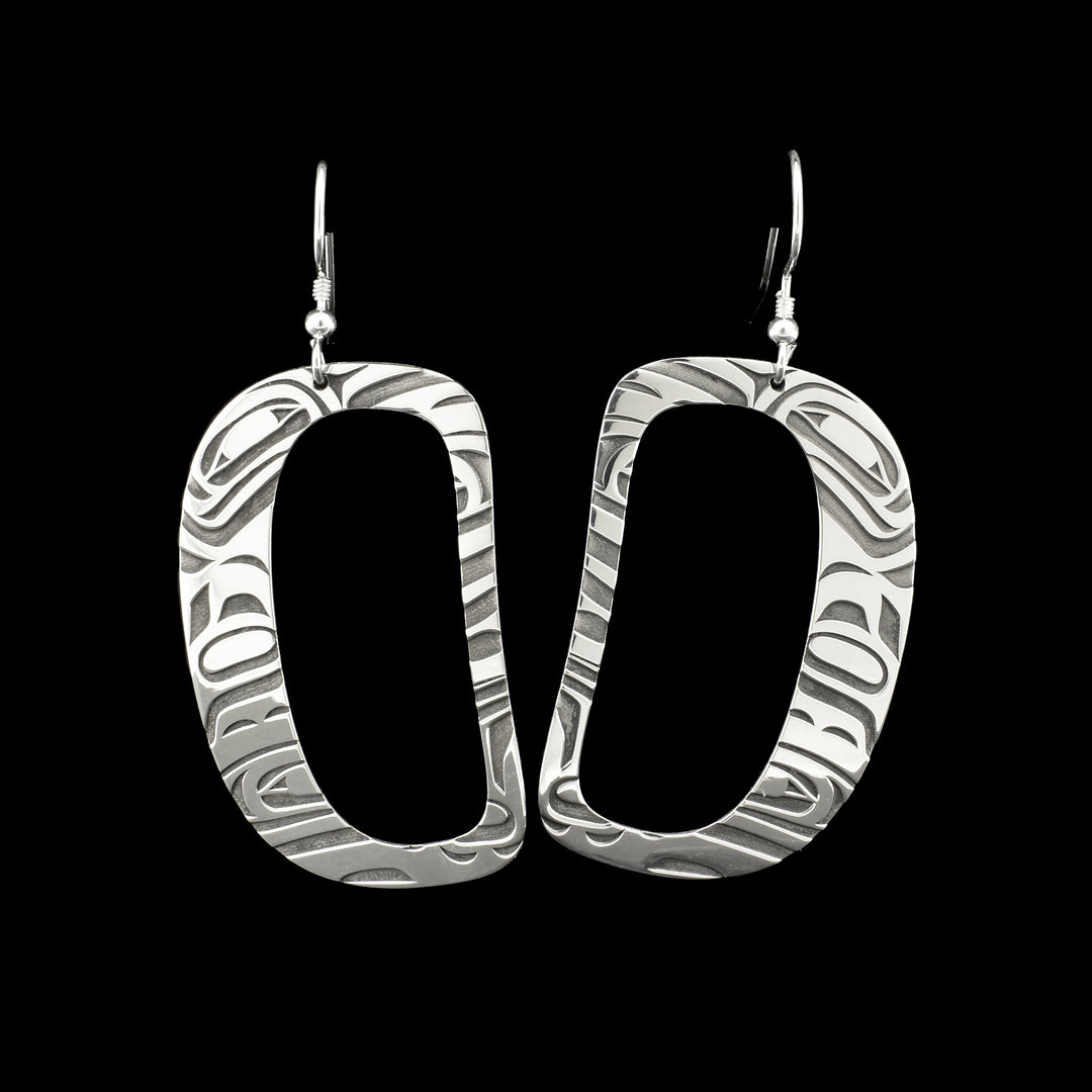 These dangling Orca earrings are made from sterling silver and have large, oval shaped hangs. There are large cutouts in the middle of the hangs and there are carvings on them that depict the Orca.