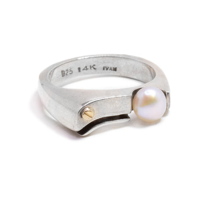 a sterling silver band with a flat side. There is a pearl on one side of the flat area, and a gold detail on the other side.