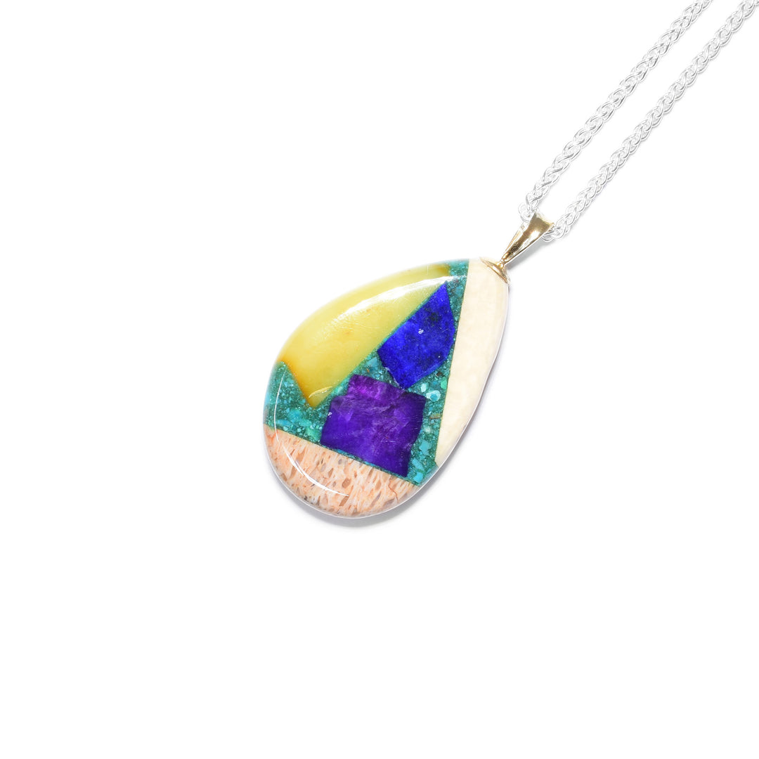 Uneven teardrop shape. This gemstone pendant is a mosaic of ammolite, lapis, malachite, turquoise, sugilite, rhodochrosite, red coral, amber, mammoth ivory and gold nuggets. 14K gold bail.