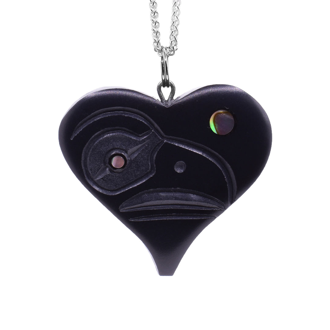This argillite and abalone pendant is heart shaped and made of argillite. There are carvings of the Raven carved into the surface of it and abalone set into the eyes of the Raven.