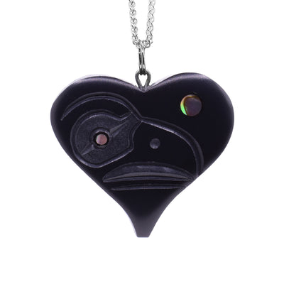 This argillite and abalone pendant is heart shaped and made of argillite. There are carvings of the Raven carved into the surface of it and abalone set into the eyes of the Raven.