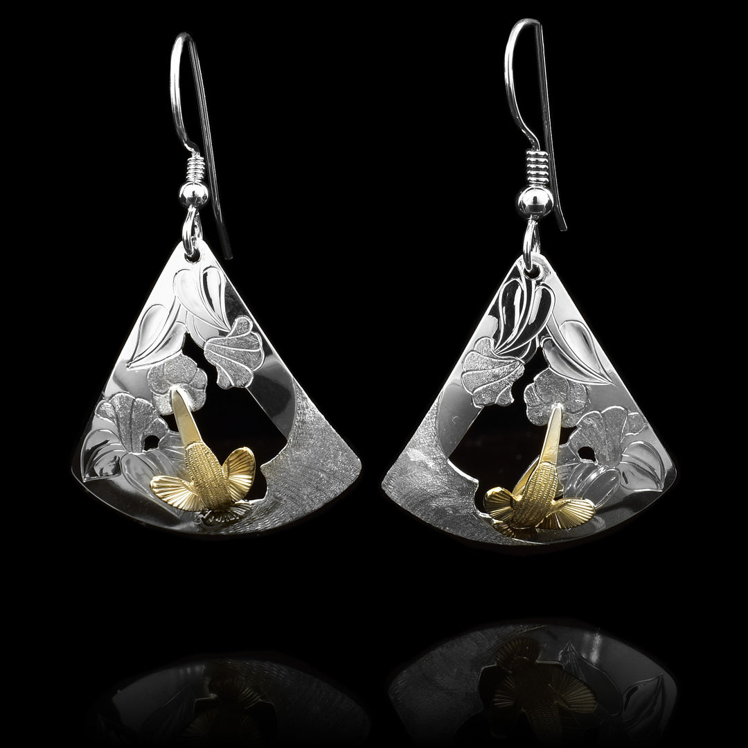 These Hummingbird earrings gold have sterling silver hangs that are wide and triangular. The silver hangs have carvings and cutouts depicting foliage and flowers and there are carved, 14K gold Hummingbirds mounted in the center of the hangs.