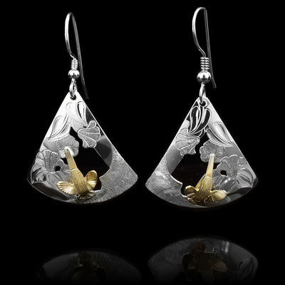 These Hummingbird earrings gold have sterling silver hangs that are wide and triangular. The silver hangs have carvings and cutouts depicting foliage and flowers and there are carved, 14K gold Hummingbirds mounted in the center of the hangs.