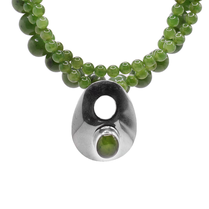 This beaded pendant necklace has three beaded necklaces with different sized jade beads on them that are stacked together. There is a sterling silver pendant has a teardrop shape with a jade bead below a cutout on the pendant.