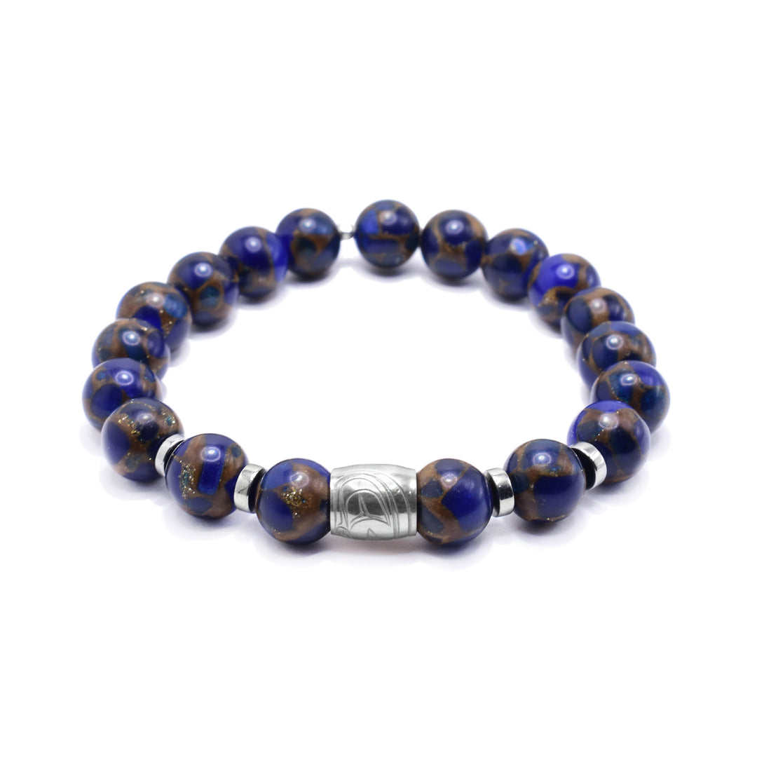 This gemstone charm bracelet has small, sphere shaped beads made from jasper. The beads have a blue color with brown highlights. There is a sterling silver spirit bead in the center of the piece with a depiction of the head of the Eagle carved into it. There are round, flat silver spacers (two on either side of the spirit bead).