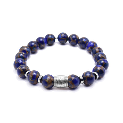 This gemstone charm bracelet has small, sphere shaped beads made from jasper. The beads have a blue color with brown highlights. There is a sterling silver spirit bead in the center of the piece with a depiction of the head of the Eagle carved into it. There are round, flat silver spacers (two on either side of the spirit bead).