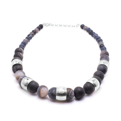 This chunky dark agate necklace has sphere shaped gemstone beads that are larger at the bottom portion of the piece and smaller at the tops of it. There are five sterling silver spirit beads that are ditributef through the large beads. The spirit beads have depictions of the Bear, the Orca, the Hummingbird, the Sun and the Frog carved into the surface of them.