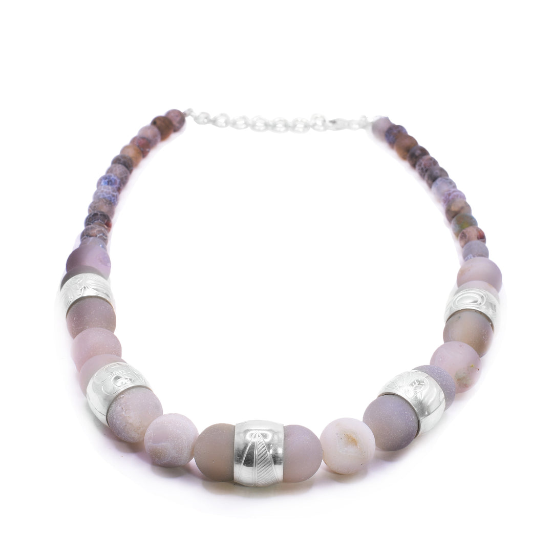 This chunky pink agate necklace has sphere shaped gemstone beads that are larger at the bottom portion of the piece and smaller at the tops of it. There are five sterling silver spirit beads that are ditributef through the large beads. The spirit beads have depictions of the Hummingbird, the Sun, the Swan, a dragonfly and a feather carved into the surface of them.