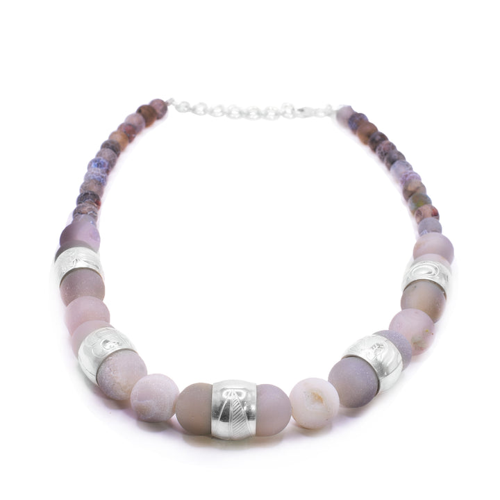 This chunky pink agate necklace has sphere shaped gemstone beads that are larger at the bottom portion of the piece and smaller at the tops of it. There are five sterling silver spirit beads that are ditributef through the large beads. The spirit beads have depictions of the Hummingbird, the Sun, the Swan, a dragonfly and a feather carved into the surface of them.