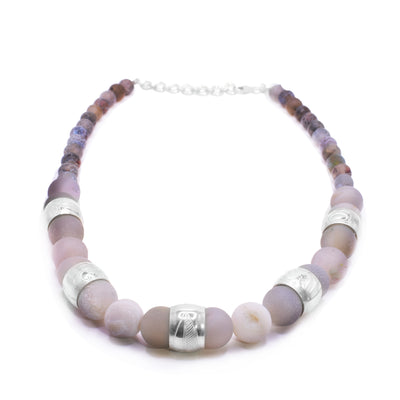 This chunky pink agate necklace has sphere shaped gemstone beads that are larger at the bottom portion of the piece and smaller at the tops of it. There are five sterling silver spirit beads that are ditributef through the large beads. The spirit beads have depictions of the Hummingbird, the Sun, the Swan, a dragonfly and a feather carved into the surface of them.