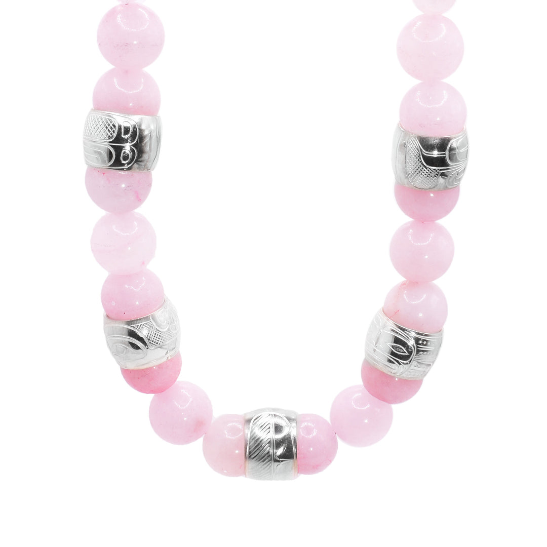 This chunky rose quartz necklace has sphere shaped gemstone beads that are larger at the bottom portion of the piece and smaller at the tops of it. There are five sterling silver spirit beads that are ditributef through the large beads. The spirit beads have depictions of the Hummingbird, the Sun, the Swan, a dragonfly and a feather carved into the surface of them.