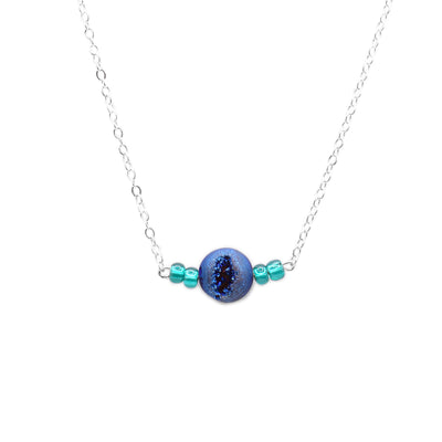 This blue agate necklace has a sterling silver chain with a large, spherical agate pendant with two glass beads to either side of it. The glass beads are turquoise and the agate ball is textured.