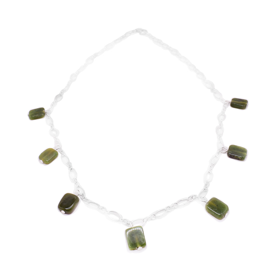 This jade charm necklace has a simple sterling silver chain with seven jade pieces dangling from the bottom half of the piece. The jade beads are small, flat and rectangle shaped.