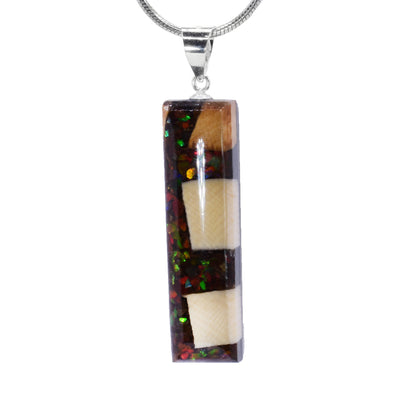 This ivory pendant is made from ammolte gemstone and fossilized mammoth ivory and has a thin, rectangle shape. Chunks of ammolite and ivory have been set into resin and form the pendant.