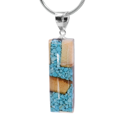 This turquoise pendant is made from fossilized mammoth ivory and turquoise gemstones. Pieces of turquoise and chunks of ivory have been set in resin and shaped into a thin rectangle.