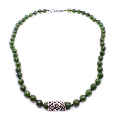 A necklace with round jade beads that has knots in between every bead. There is a sterling silver pendant in the middle. It is tubular in shape, and has a handcarved design on it.