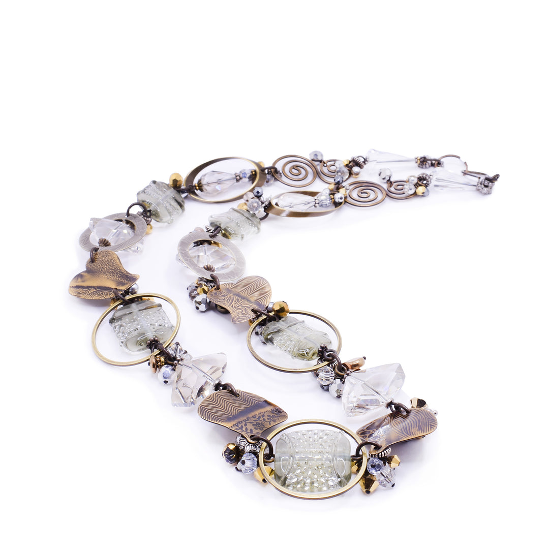 This beautiful beaded necklace is made up of many gemstones that are clear, white, and grey in colour with contrasting brass accents, giving it a stunning appearance that resembles a foggy morning sky.