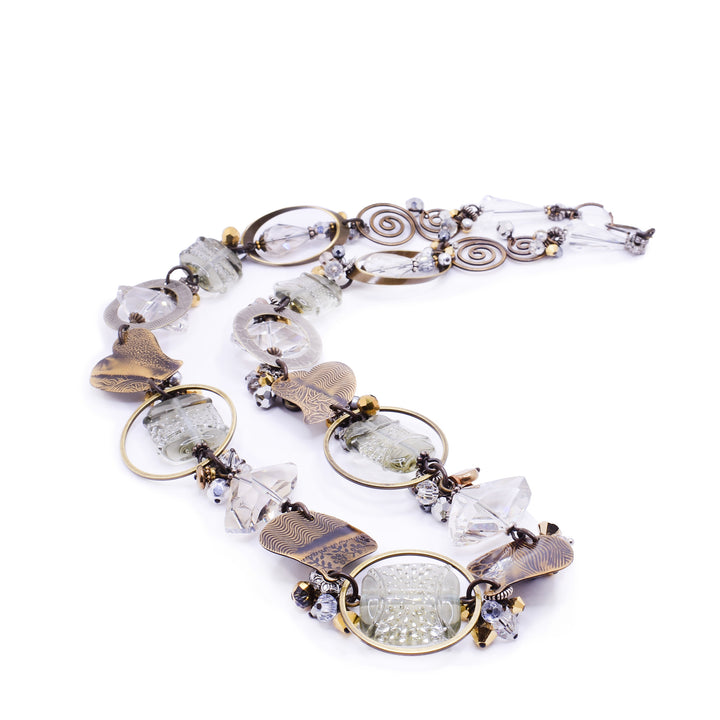 This beautiful beaded necklace is made up of many gemstones that are clear, white, and grey in colour with contrasting brass accents, giving it a stunning appearance that resembles a foggy morning sky.