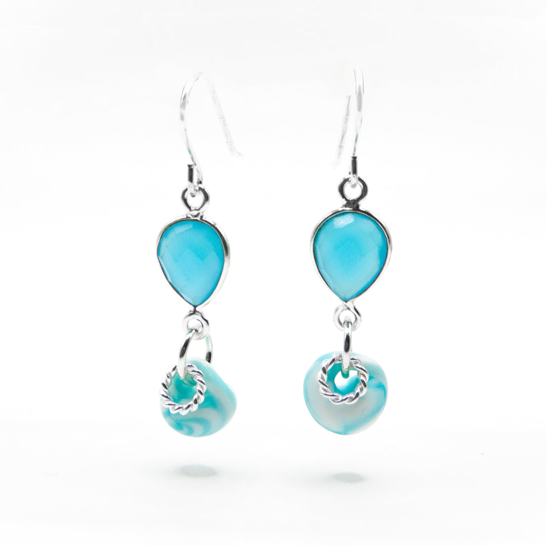 Faceted, downward teardrop-shaped blue chalcedony dangles from hooks. Blue and white glass adornment and silver ring adornment dangle below gemstone. All metal is sterling silver.